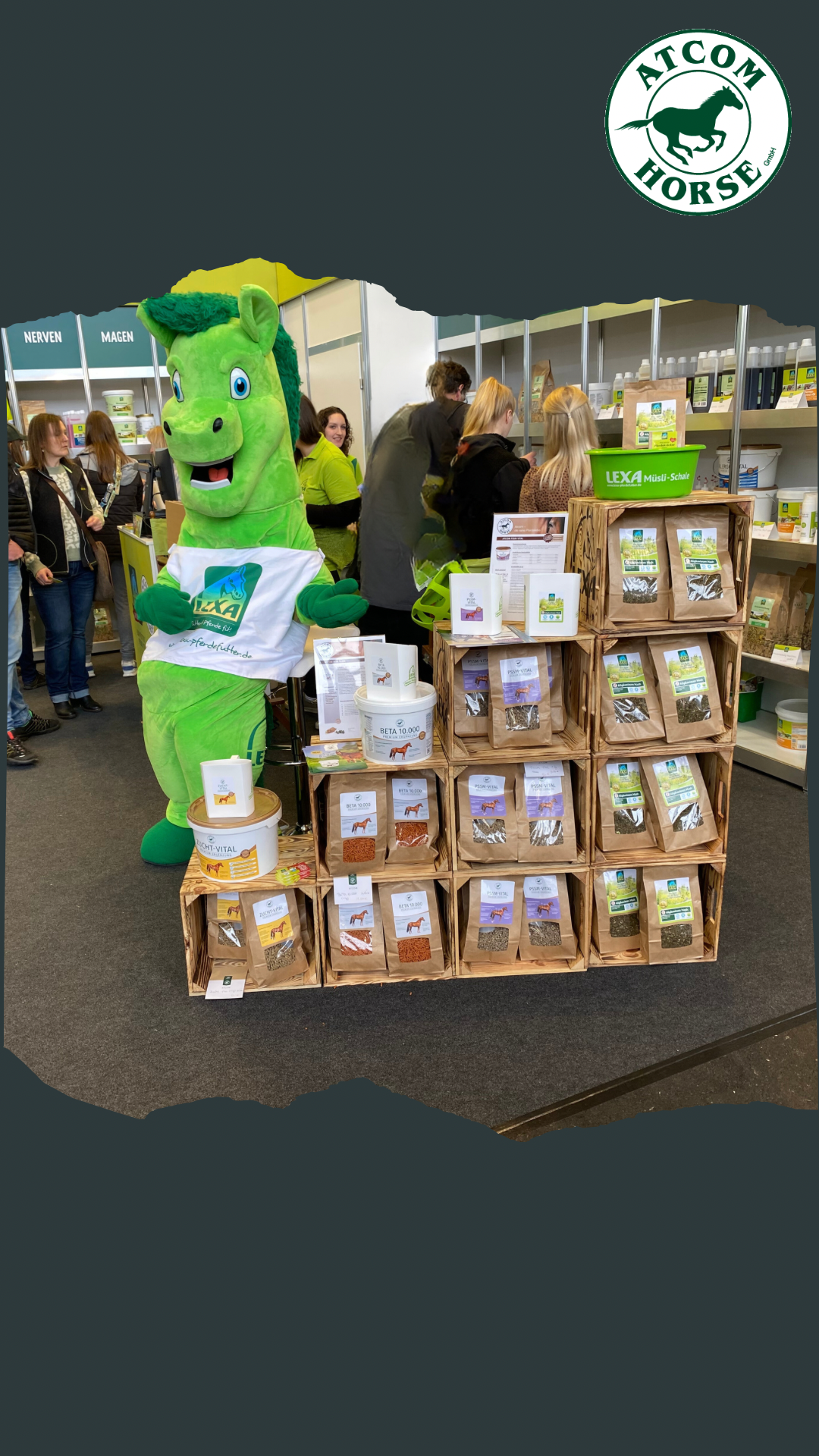 Ein grünes Maskottchen in Form eines Pferdes steht neben einem Regal mit verschiedenen Produkten für Pferde. Im Hintergrund sind Menschen zu sehen.