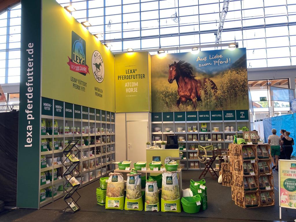 Messestand von LEXA Pferdefutter mit Regalen voller Produkte und einem großen Plakat eines Pferdes im Hintergrund.