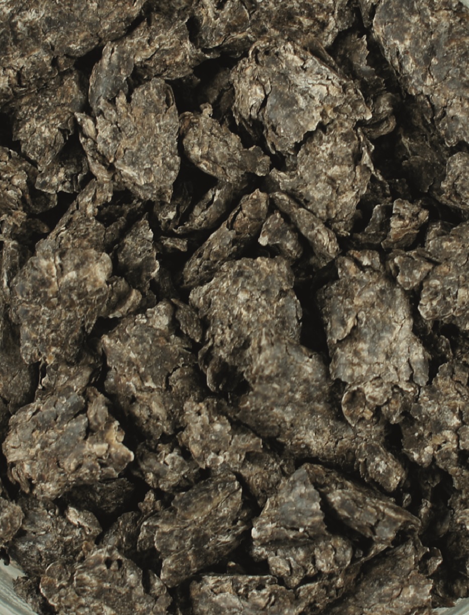 Dunkle, zerbrochene Stücke von getrocknetem Material, möglicherweise Pflanzenreste oder Futter.